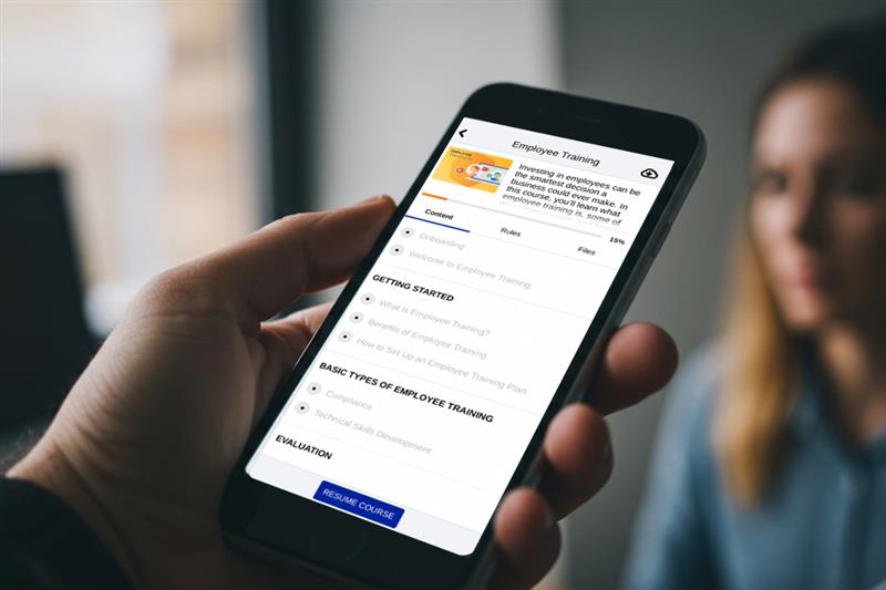Person holding a smartphone displaying an LMS for employee training course interface with modules and progress tracking.