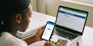 A student uploading documents on her phone while completing a university form on a laptop through an apply portal for universities.