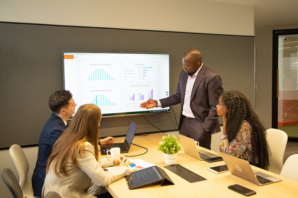 Education team reviewing student performance charts and course data on a smart screen to monitor progress and decision-making in virtual education
