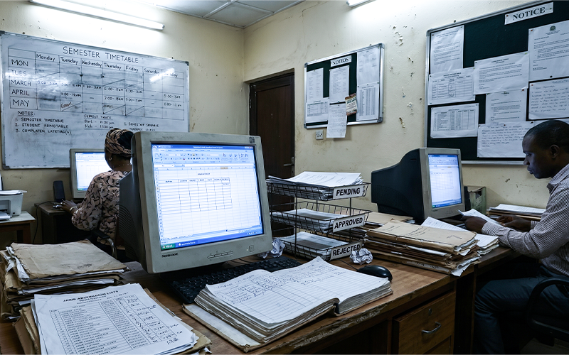 Small university administrative team manually managing admissions, spreadsheets, classroom schedules, and student records with limited digital systems; visual showing operational limitations before scalable infrastructure adoption